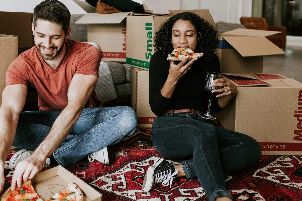 Two people eating pizza after moving into their new home.